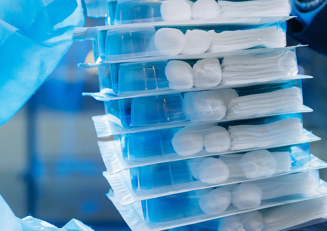 Une personne portant des gants tient une pile de petites boîtes contenant de l’équipement médical, comme des tampons, des bandages.