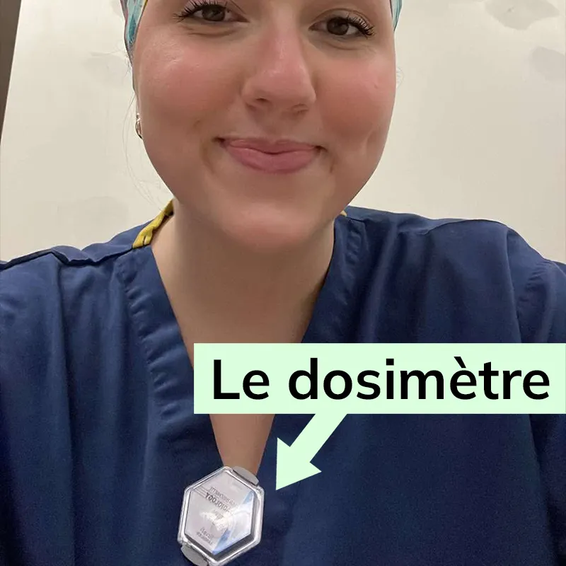 Emma Bissonnette portant un petit chapeau couvrant ses cheveux. Un dosimètre est accroché à son vêtement.